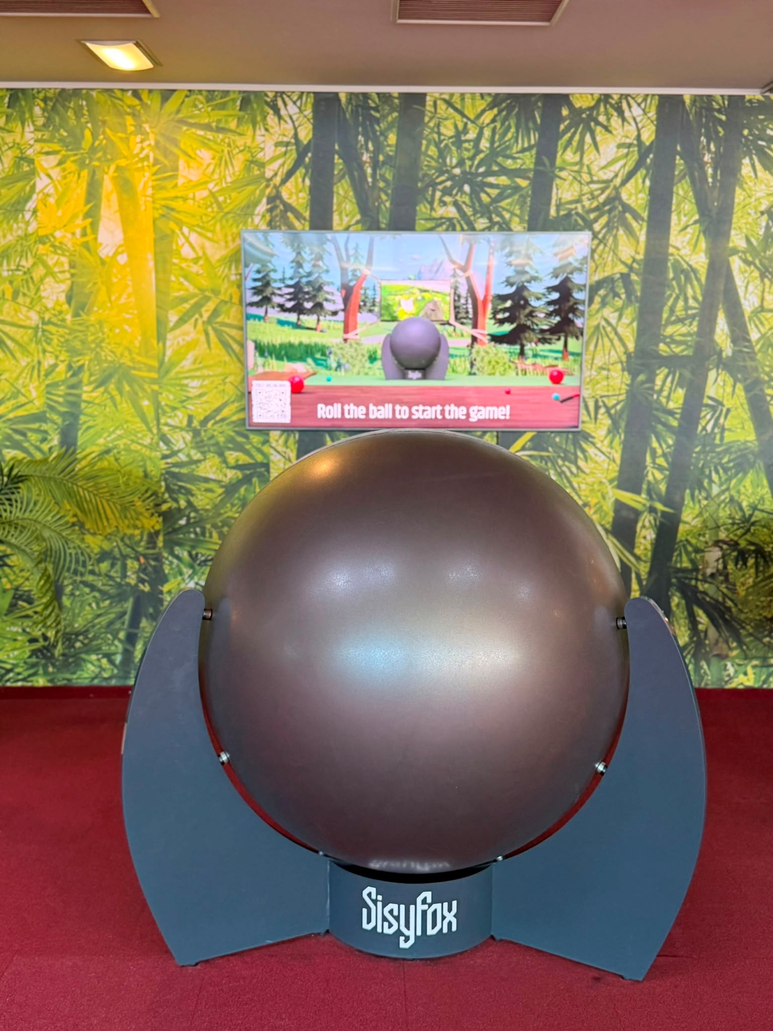 SisyFox-Spielstation im Monki Park mit großer Kugel, Bildschirm und interaktivem Ballspiel vor einer Dschungelkulisse.